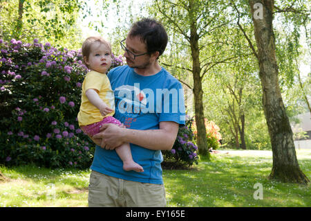 Baby girl being held by her father looking tearful Stock Photo