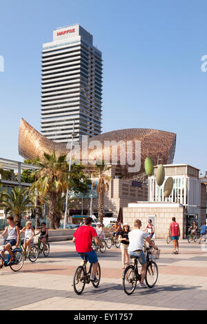 People cycling along the Passeig Maritim, with fish sculpture in the background, Barceloneta, Barcelona Spain Europe Stock Photo