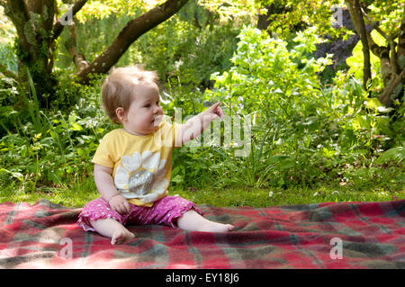 Baby girl sitting unaided on a rug pointing Stock Photo