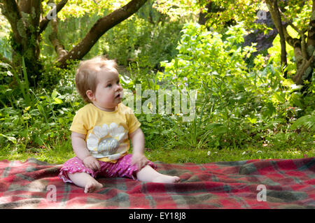 Baby girl sitting unaided on a rug outdoors Stock Photo