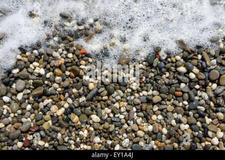 Close-up view of wet beach pebble of various colors in bubbles of surf foam as a background. Stock Photo