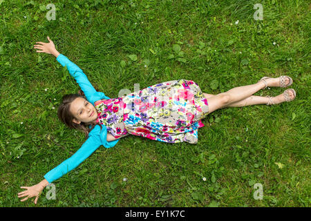 Cute little girl lying on the grass, arms outstretched, top view. Stock Photo