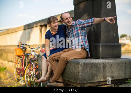Happy young couple. Couple in love emotionally talking sitting on the urban stone waterfront. Stock Photo
