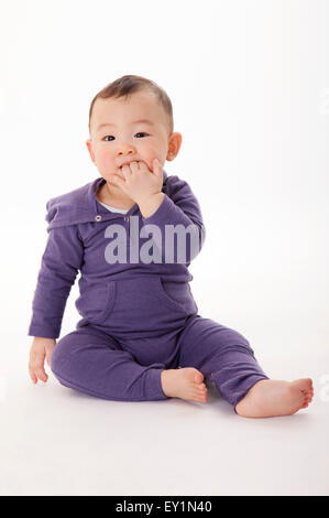 Baby boy sitting with fingers in mouth, Stock Photo