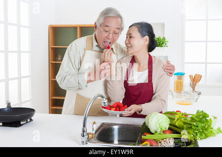 Senior couple eating food in the kitchen and smiling happily,