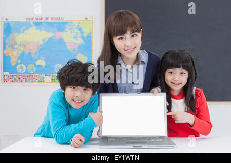 Young teacher and students holding laptop and smiling at the camera, Stock Photo
