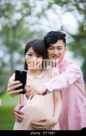 Young man and pregnant woman looking at the mobile phone and taking pictures with smile, Stock Photo