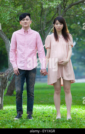 Young man and pregnant woman standing on the lawn and holding hands together, Stock Photo