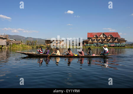 Local women in a wooden boat paddling on Inle Lake, stilt houses behind, Inle Lake, Shan State, Myanmar Stock Photo