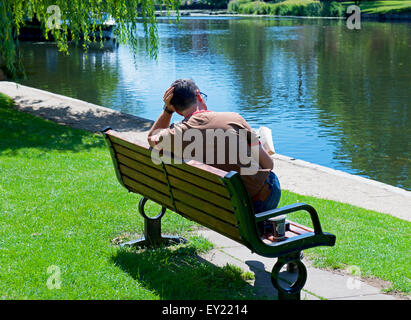 Man sitting on bench, reading a book, next to the River Avon, Stratford upon Avon, Warwickshire, England UK Stock Photo