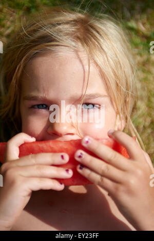 Portrait of little child blond girl with slice of watermelon, lying on green grass lawn, summer, relax Stock Photo