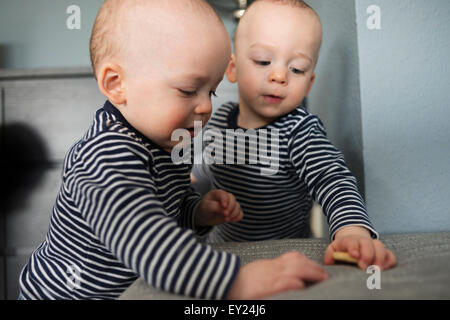 Baby twin brothers playing with biscuits in living room Stock Photo