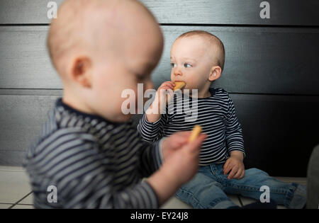 Baby twin brothers eating biscuits in living room Stock Photo