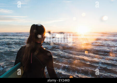 Rear view of female surfer wading into sea at sunset, Cardiff-By-The-Sea, California, USA Stock Photo