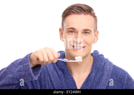 Young man in a blue bathrobe brushing his teeth with a toothbrush and looking at the camera isolated on white background Stock Photo