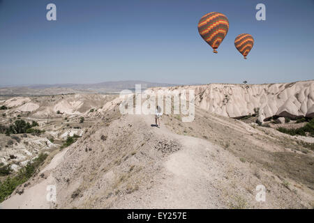 Female tourist and hot air balloons in rock formation landscape, Cappadocia, Anatolia, Turkey Stock Photo