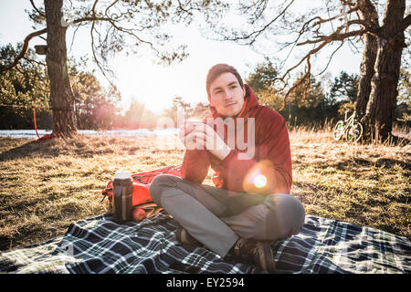Young man sitting on picnic blanket drinking coffee in forest Stock Photo