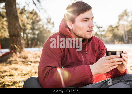 Young man sitting drinking coffee at lakeside Stock Photo