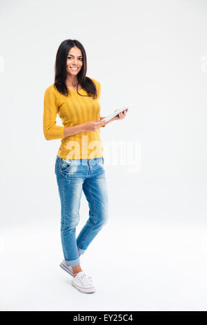Full length portrait of a happy woman standing and holding tablet computer isolated on a white background. Looking at camera Stock Photo