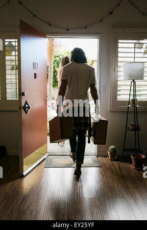 Rear view of young couple carrying suitcases out of front door Stock Photo