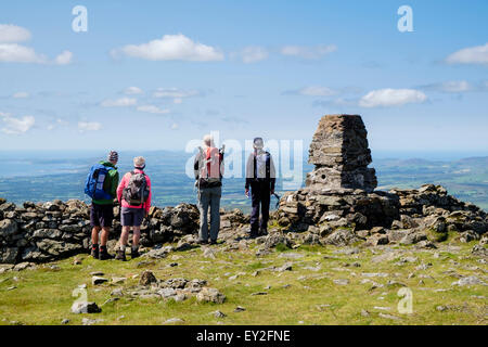 Four hikers looking west at view by trig point cairn on Moel Hebog mountain summit in mountains of Snowdonia Wales UK Stock Photo