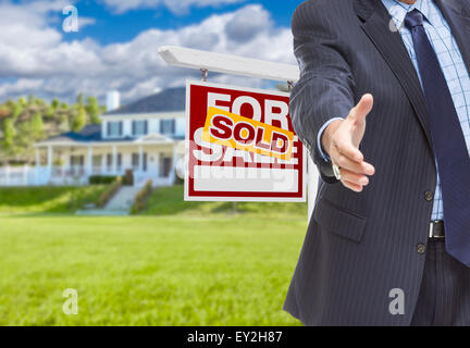 Real Estate Agent Reaches for Handshake with Sold Sign and New House Behind. Stock Photo