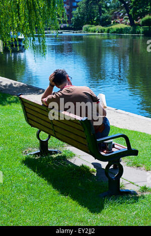Man sitting on bench, reading book, by River Avon, Stratford upon Avon, Warwickshire, England UK Stock Photo