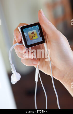 Close up of an Apple iPod nano, with headphones, held in a womans hand showing the iTunes music screen. Stock Photo
