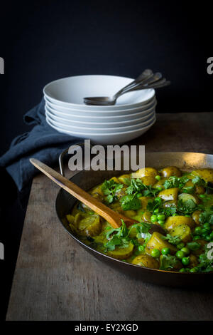 Pea & potato curry in iron casserole on wooden table Stock Photo