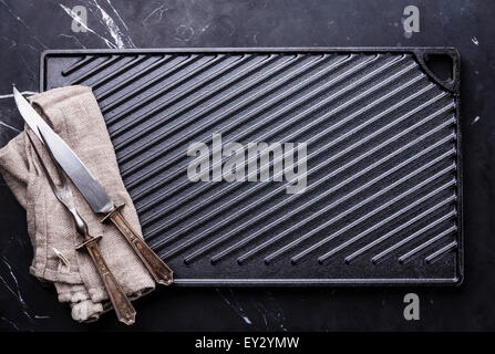 Black cast iron grill surface and fork and knife carving set on marble background Stock Photo