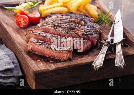 Sliced medium rare grilled Steak Ribeye with french fries on serving board block on wooden background Stock Photo