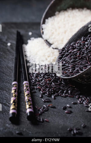 Black and white rice in old metal china bowls with black chopsticks over black slate background Stock Photo