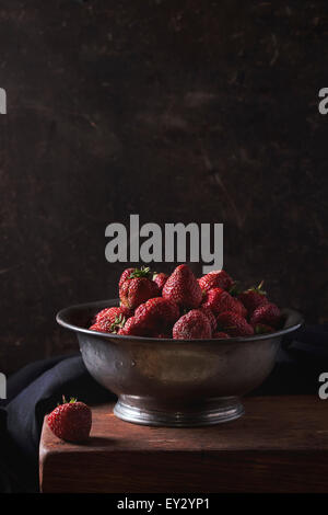 Vintage metal bowl with fresh ripe garden strawberries on wooden table with black textile. Dark rustic style. With copy space on Stock Photo