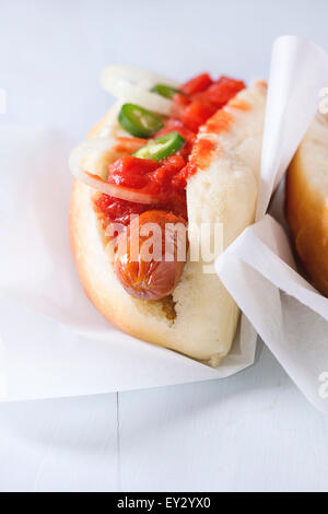 Homemade hot dogs on baking papper with tomato sauce, onion, pepper on light blue wooden background. Stock Photo