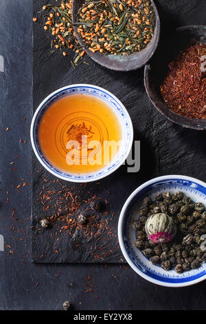 Assortment of dry tea and cup of hot tea. Green tea, black tae, green tea with rice, rooibos, dry rose buds in porcelan and old Stock Photo