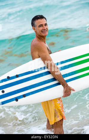 Portrait of a healthy senior male holding surfboard looking at camera on the shores of Miami Beach, Florida Stock Photo