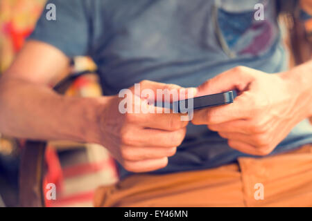 closeup of a young caucasian man sitting in a rocking chair using a smartphone in a rustic place Stock Photo