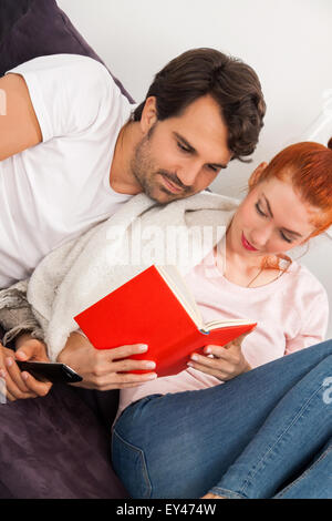 Close up Sweet Young Couple Resting at the Couch in the Living Area While Reading a Book Together Seriously. Stock Photo