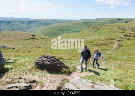 People hiking, UK countryside in Summer. Two hikers walking up the hill at Grindslow Knoll on Kinder Scout, Derbyshire, Peak District, England, UK Stock Photo