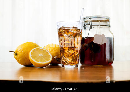 Iced Tea in Tall Glass, Lemons and Tea Jar on Wood Table Stock Photo