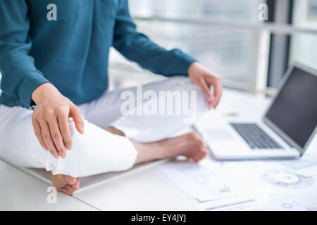 Young businesswoman doing yoga on office desk Stock Photo