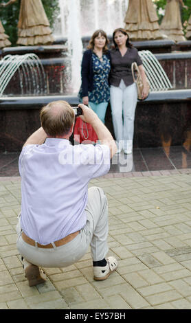 Single man takes a photo of two women as they pose at a singing fountain display in Ufa Russia in July 2015 Stock Photo