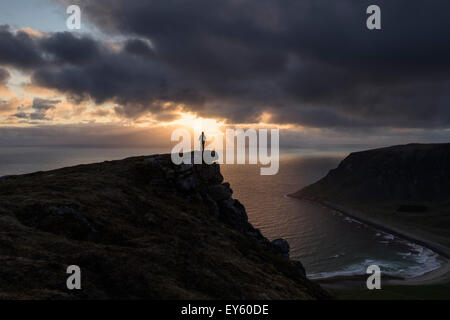 Female hiker watches midnight sun over sea from Nonstind mountain peak, Vestvågøy, Lofoten Islands, Norway Stock Photo