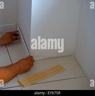 Carpenter on work putting wood skirting board with glue. Caulking Gun in Hand. .Focus is on the tools Stock Photo