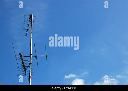 A collection of yagi television aerials on a roof against a blue sky on a sunny day with space for copy. Stock Photo