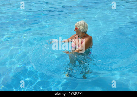 High angle full length portrait of elderly lady that standing in bright blue pool water. Stock Photo
