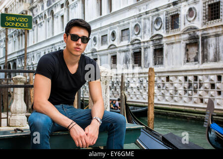 Portrait of Attractive Dark Haired Young Man Leaning Against Railing on Foot Bridge Over Narrow Canal in Venice, Italy Stock Photo