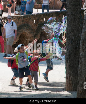 Children chasing giant bubbles created by street performer in Parc Guell, Barcelona Stock Photo