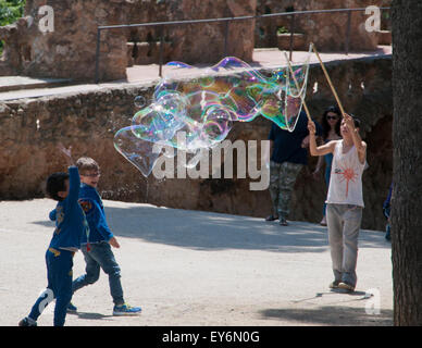 Children chasing giant bubbles created by street performer in Parc Guell, Barcelona Stock Photo