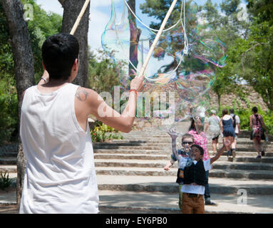 Child chasing giant bubbles created by street performer in Parc Guell, Barcelona Stock Photo